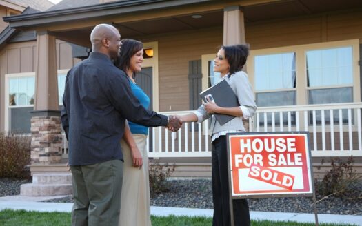 Pareja con agente inmobiliario frente a casa recien vendida